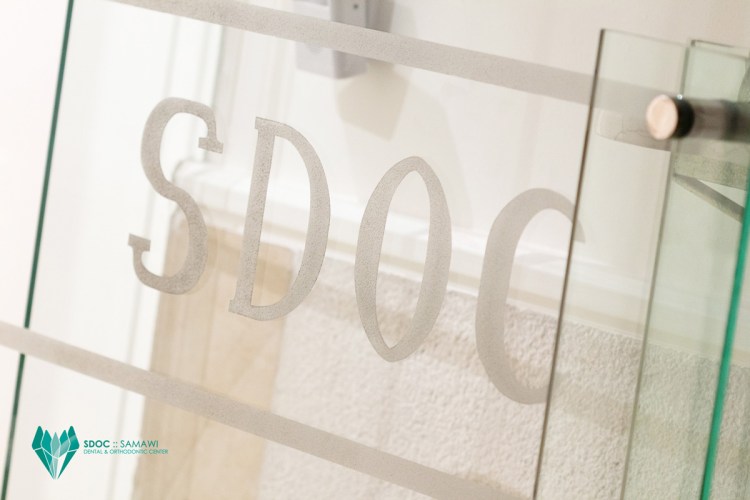 Close-up of the glass door featuring the engraved letters 'SDOC' for the Samawi Dental & Orthodontic Center.