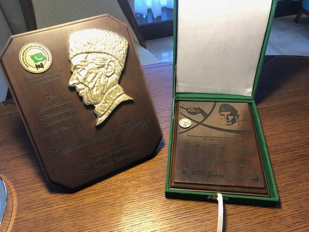 A wooden plaque with a gold relief portrait and text, awarded to Dr. Shadi Samawi at the 7th International Orthodontic Conference for Excellence Through Synergy.